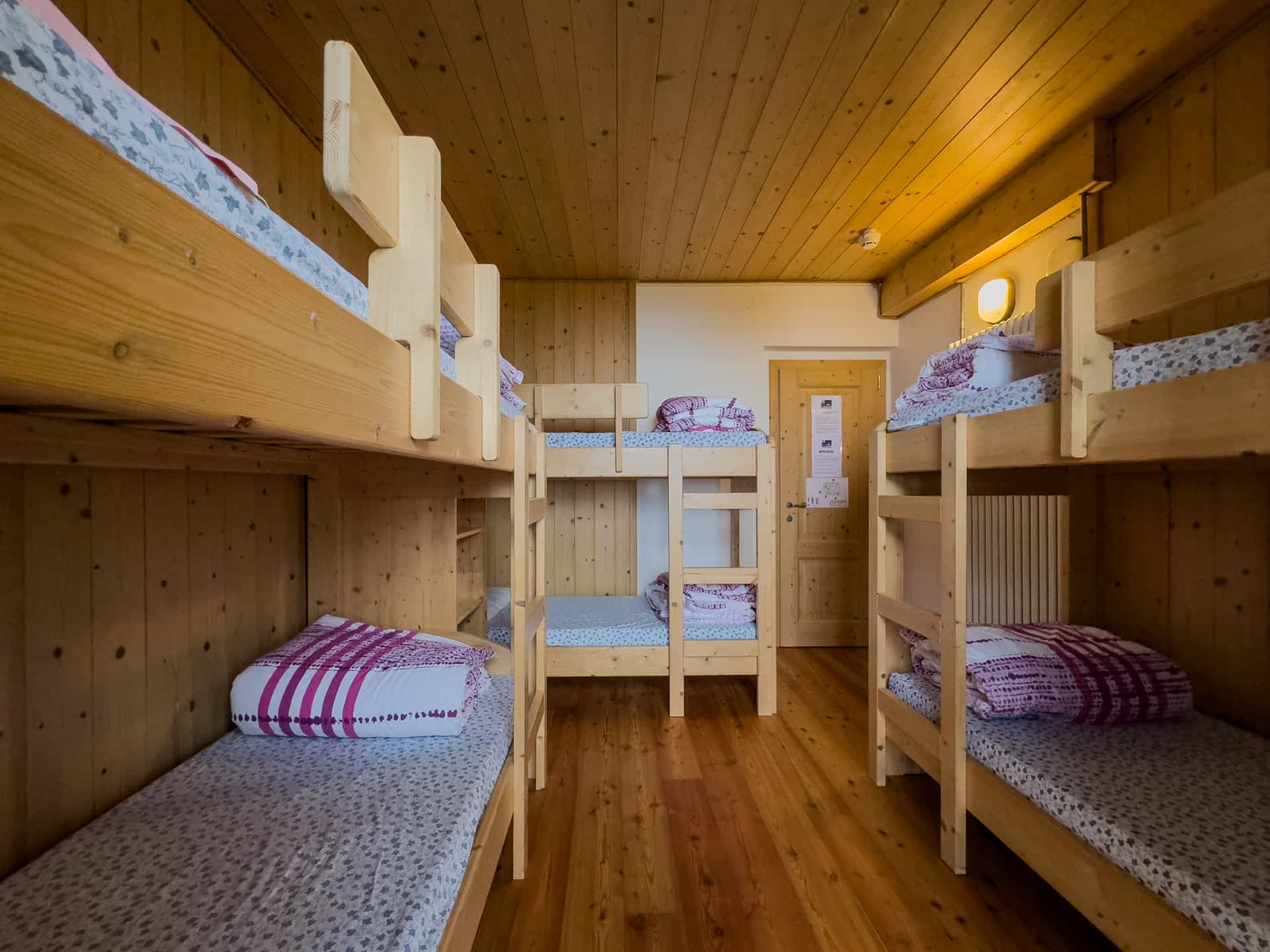 Wooden bunk beds in a rustic mountain refuge dormitory with wood-paneled walls and floor.