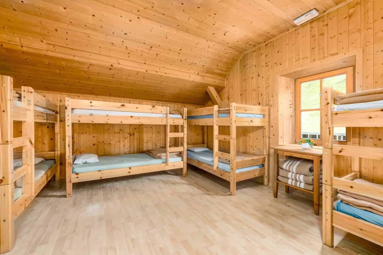 Bunk room with wooden walls and floors, featuring multiple wooden bunk beds and a window view.