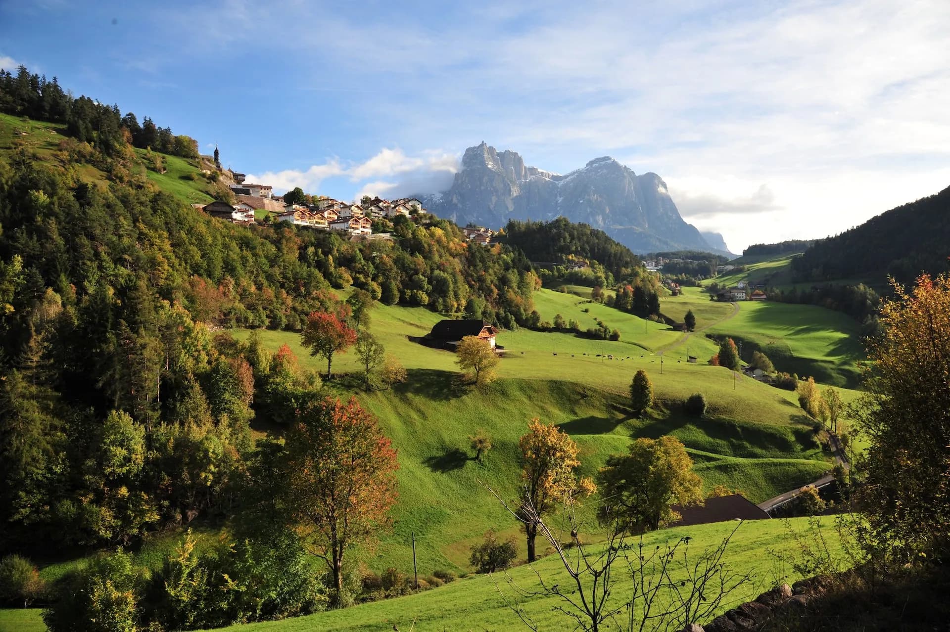 Kastelruth village nestled in green alpine valley with autumn trees and rugged mountains.