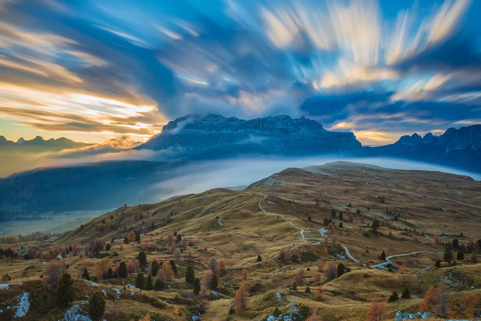 Alpine landscape with Piz Boe mountain, fog, and streaking sunset clouds in the Dolomites.
