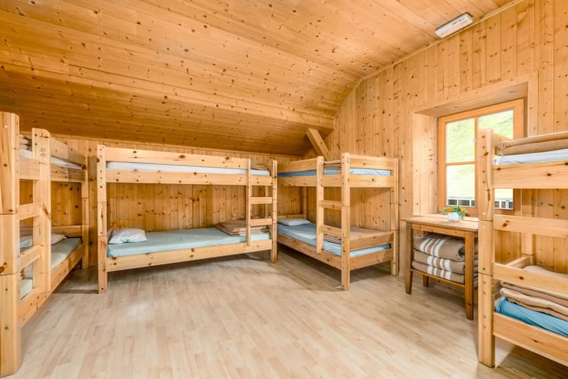 Bunk room with wooden walls and floors, featuring multiple wooden bunk beds and a window view.