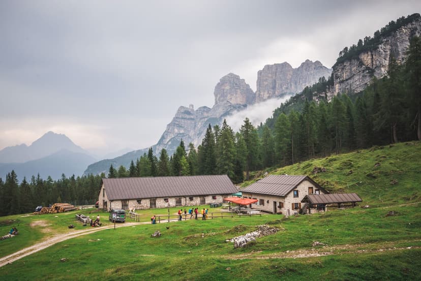 Malga Pramper mountain hut with hikers on green pasture below rugged Dolomite peaks.