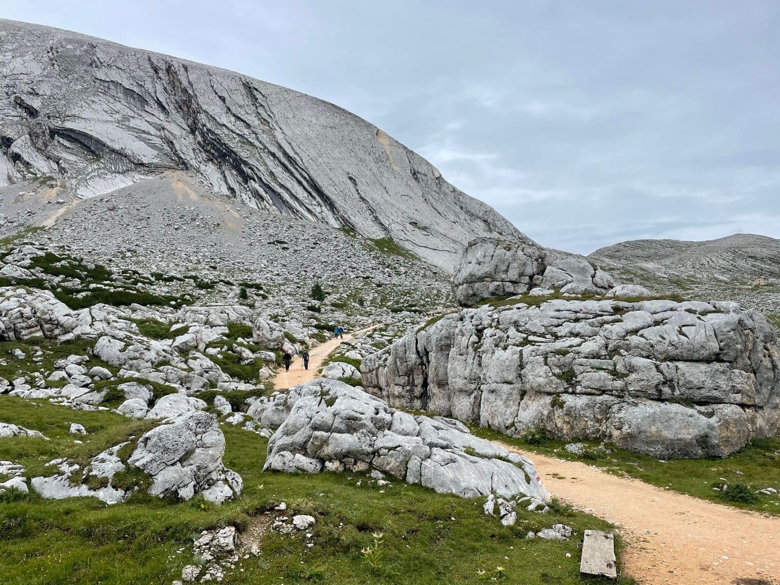 Hikers on a dirt trail through a rocky alpine mountain landscape.