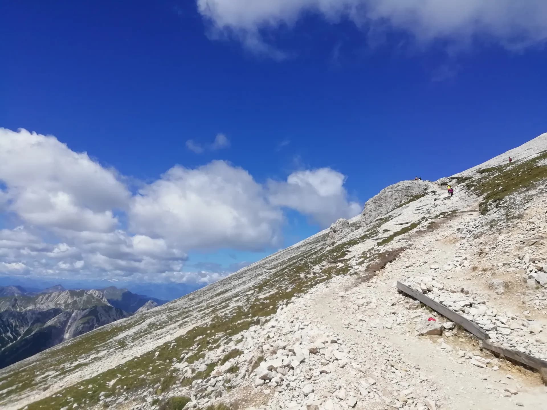 Hikers on a rocky mountain trail in the Dolomites under a blue sky with clouds.