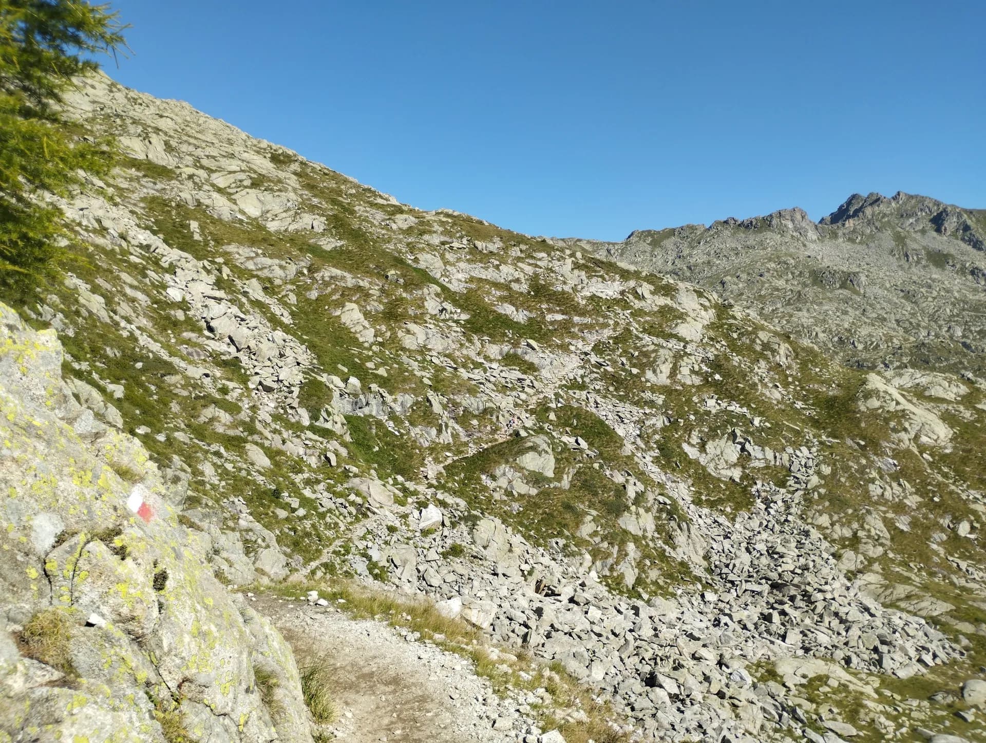 Hiking trail with red and white trail marker on rocky mountain slope in Adamello-Brenta Nature Park.