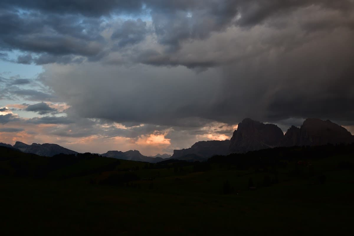 Dramatic dark storm clouds over mountain peaks and rolling green hills at sunset