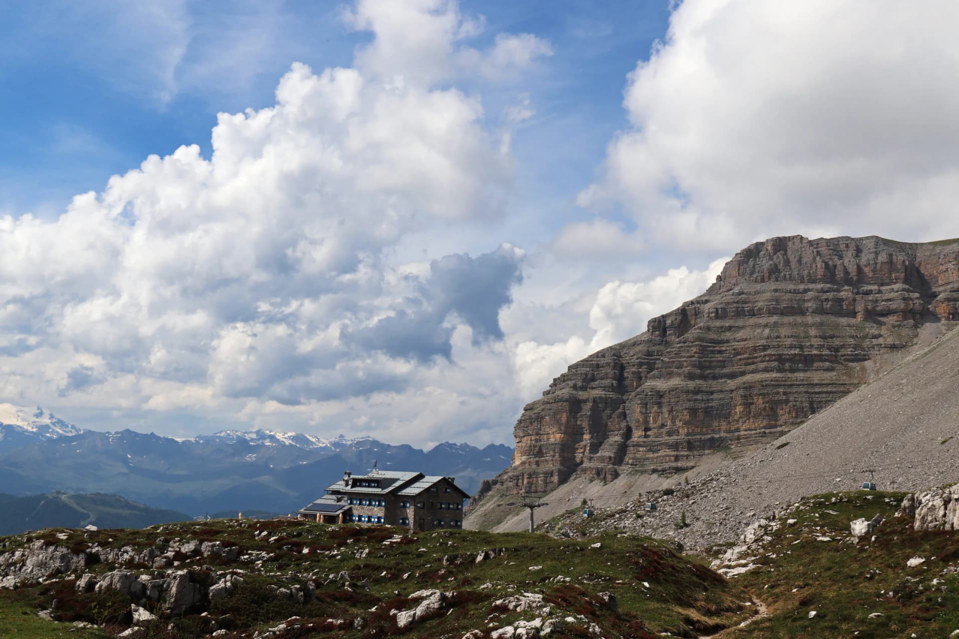 Rifugio Graffer mountain hut below a massive rock face with distant snow-capped peaks