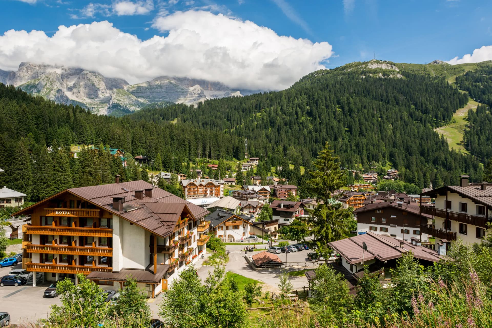Alpine village with chalet-style hotels nestled in green forest below rocky peaks in Madonna di Campiglio.