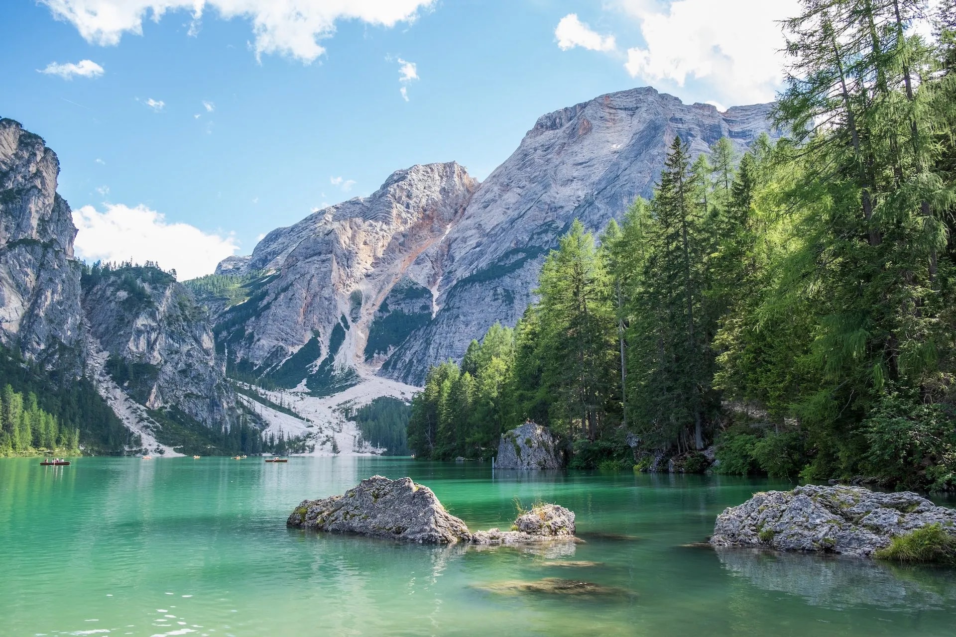 Lago di Braies with emerald water, rocky mountains, and boats on a sunny day.