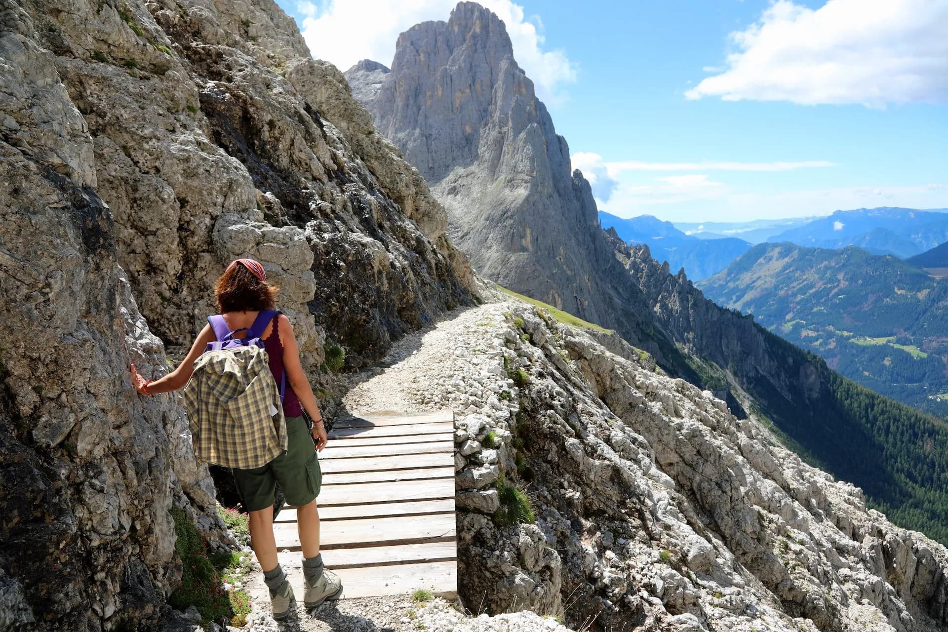 Hiker on rocky mountain trail with wooden plank section and distant peaks