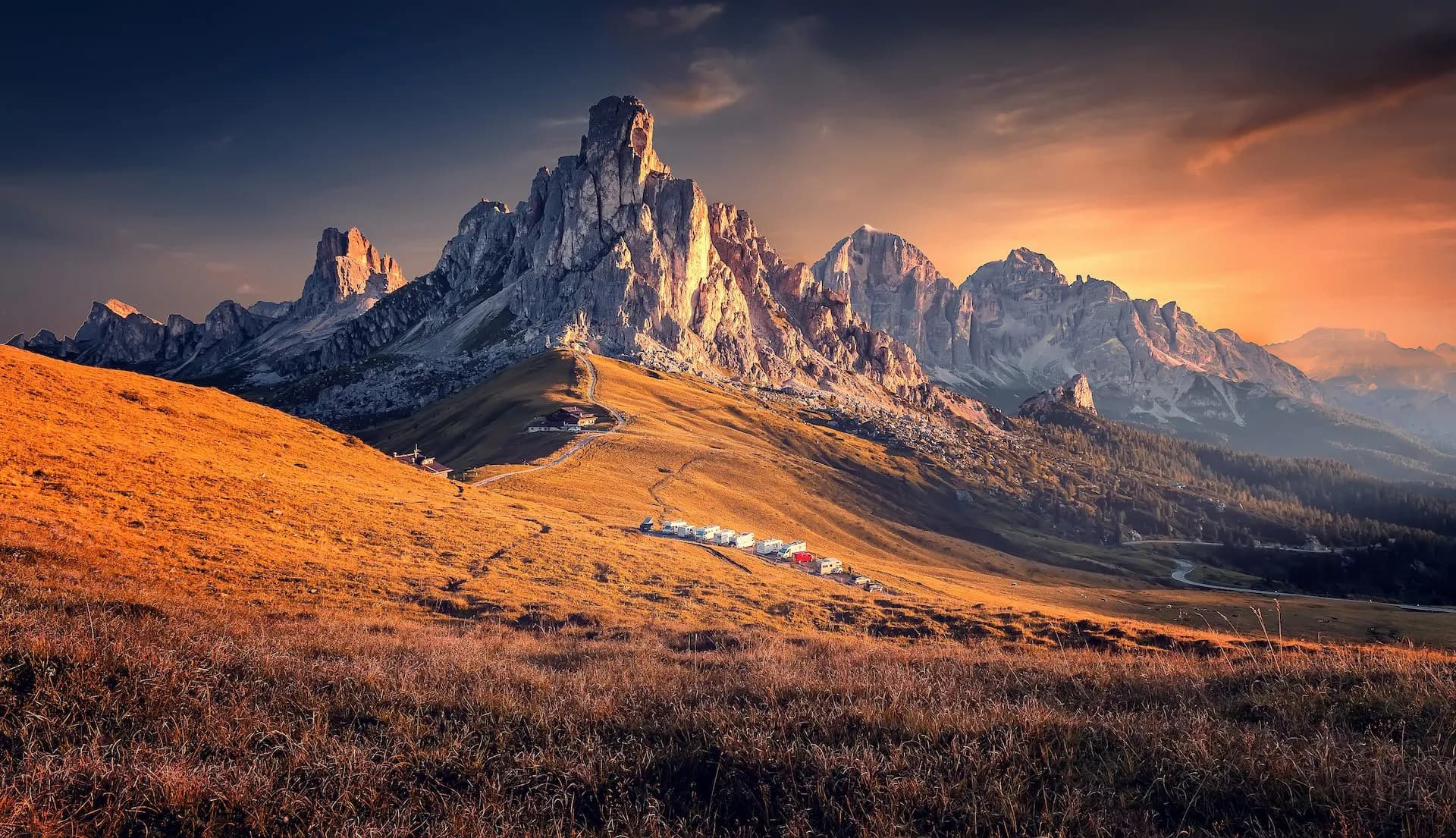 Rocky mountain peaks illuminated by sunset over golden grassy slopes near Passo Giau.