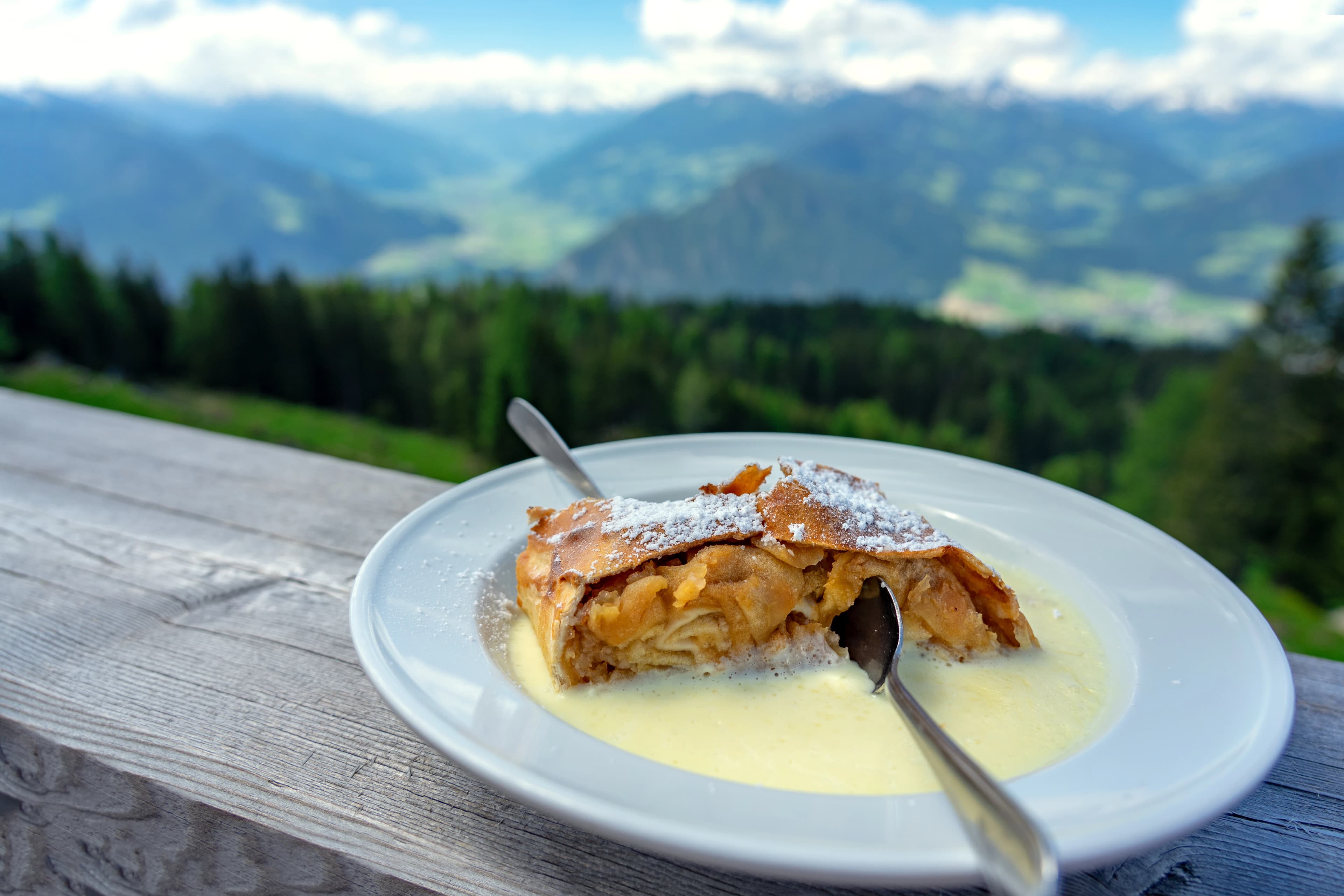 traditional apple strudel dessert with vanilla sauce in tirol alpine hut with mountain view