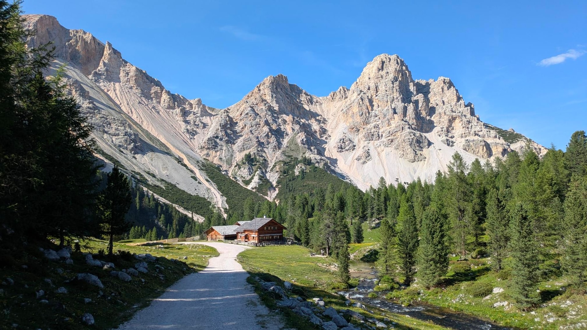Wooden mountain hut in the Fanes-Sennes-Prags Nature Park with jagged limestone peaks and pine forest.