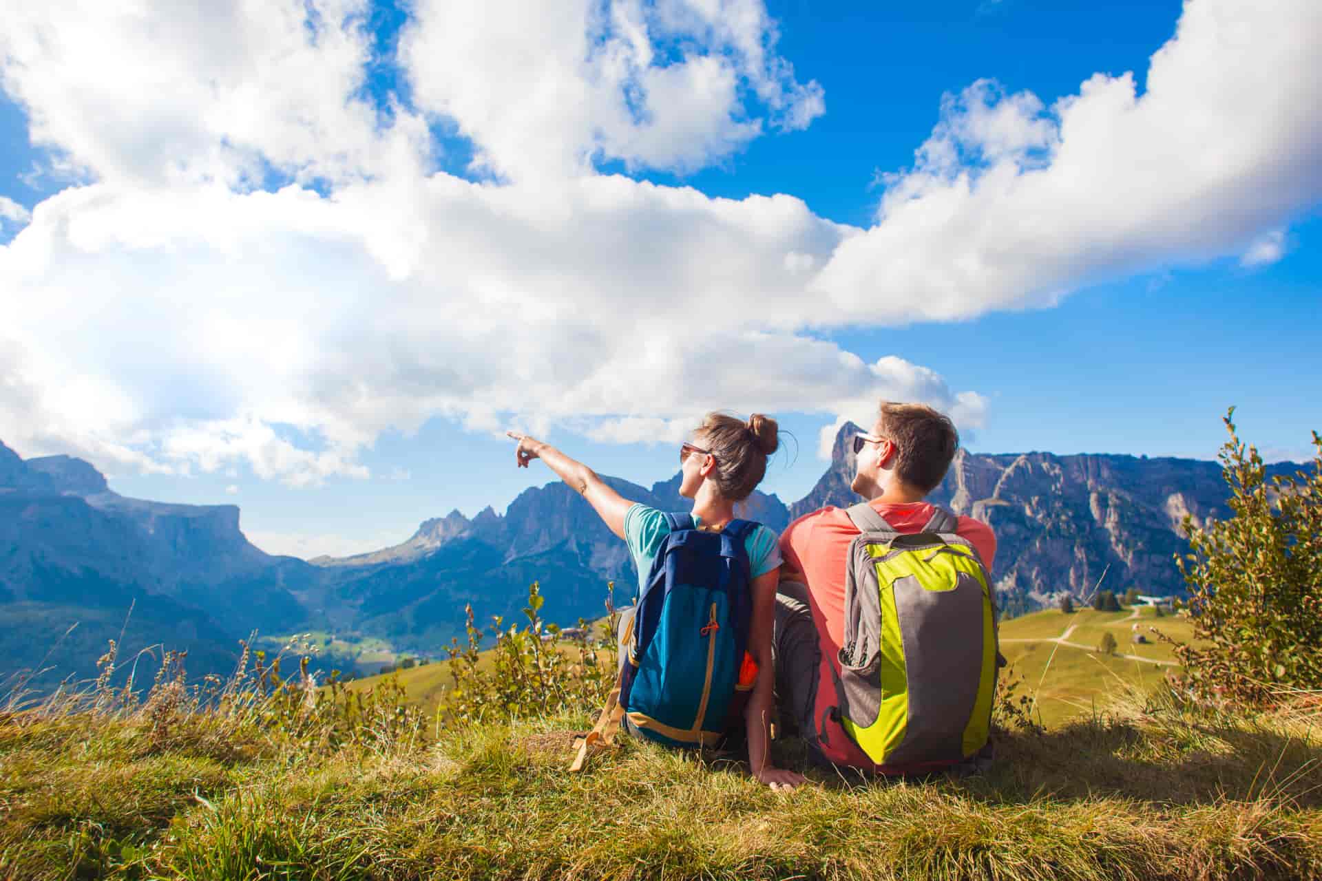 Hikers with backpacks sitting on top of a hill and enjoying mountains view. Dolomiti, Alta Badia