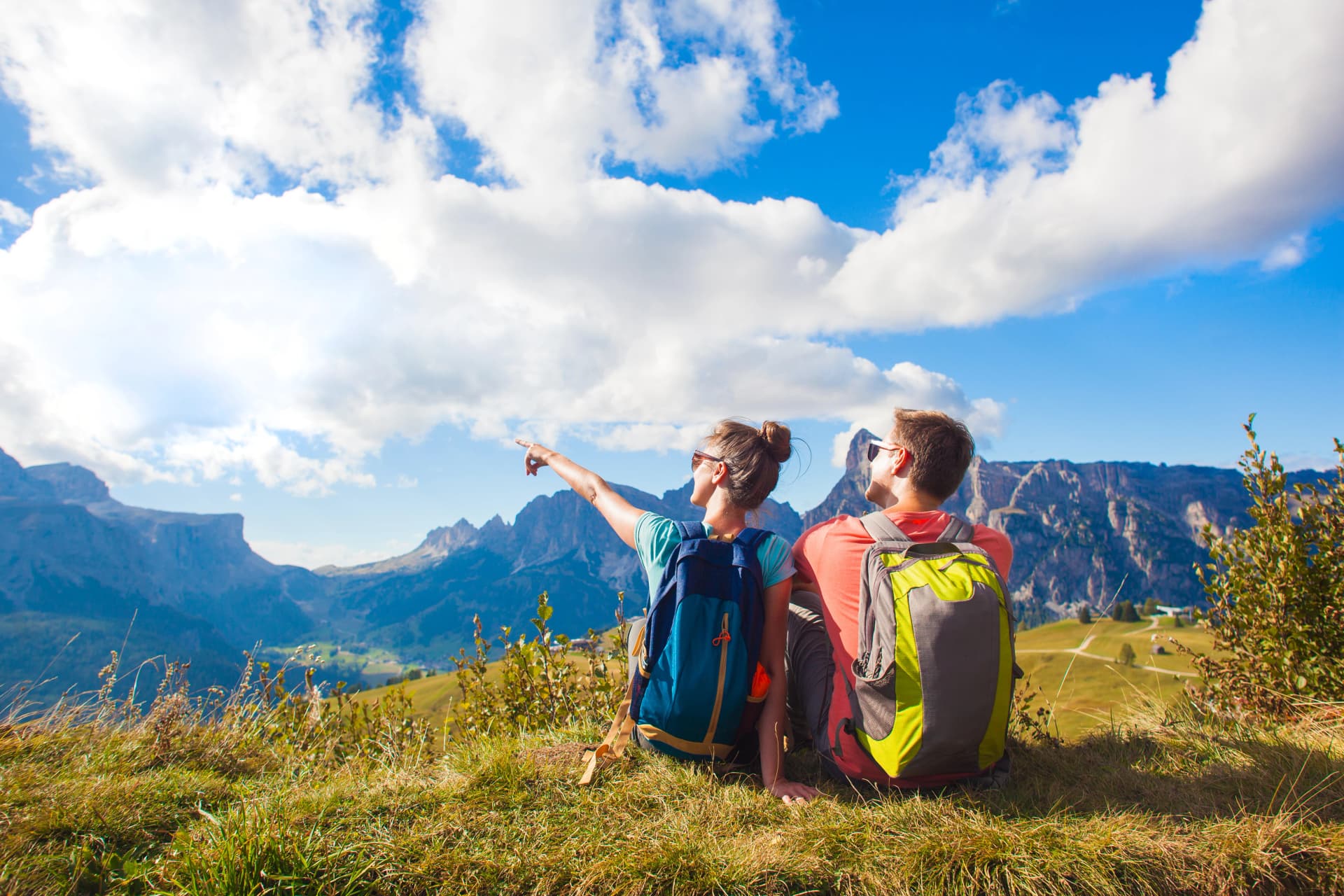 Hikers with backpacks sitting on top of a hill and enjoying mountains view. Dolomiti, Alta Badia