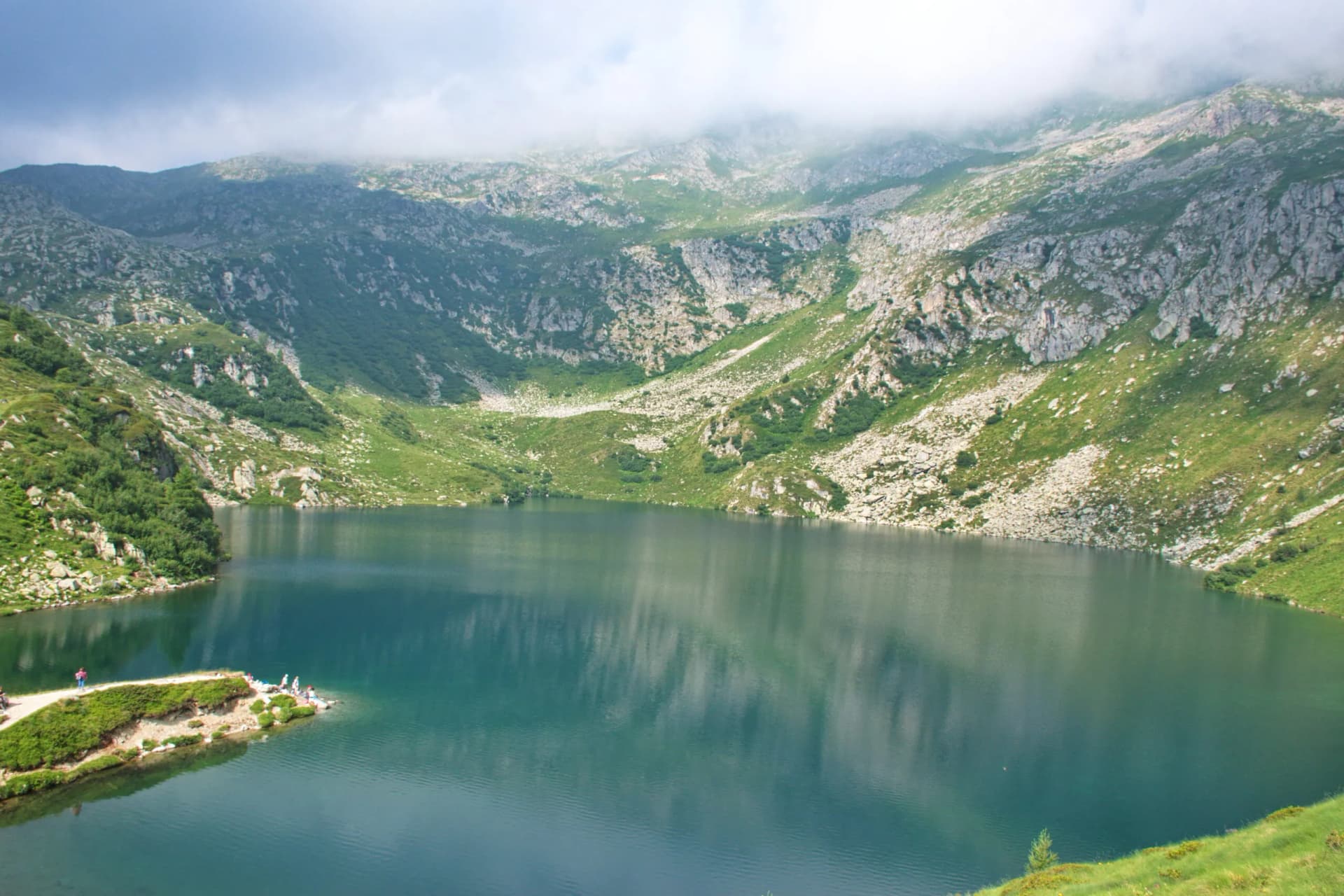 High-angle view of five lakes in Brenta Dolomites, Italy, with green slopes and misty peaks.