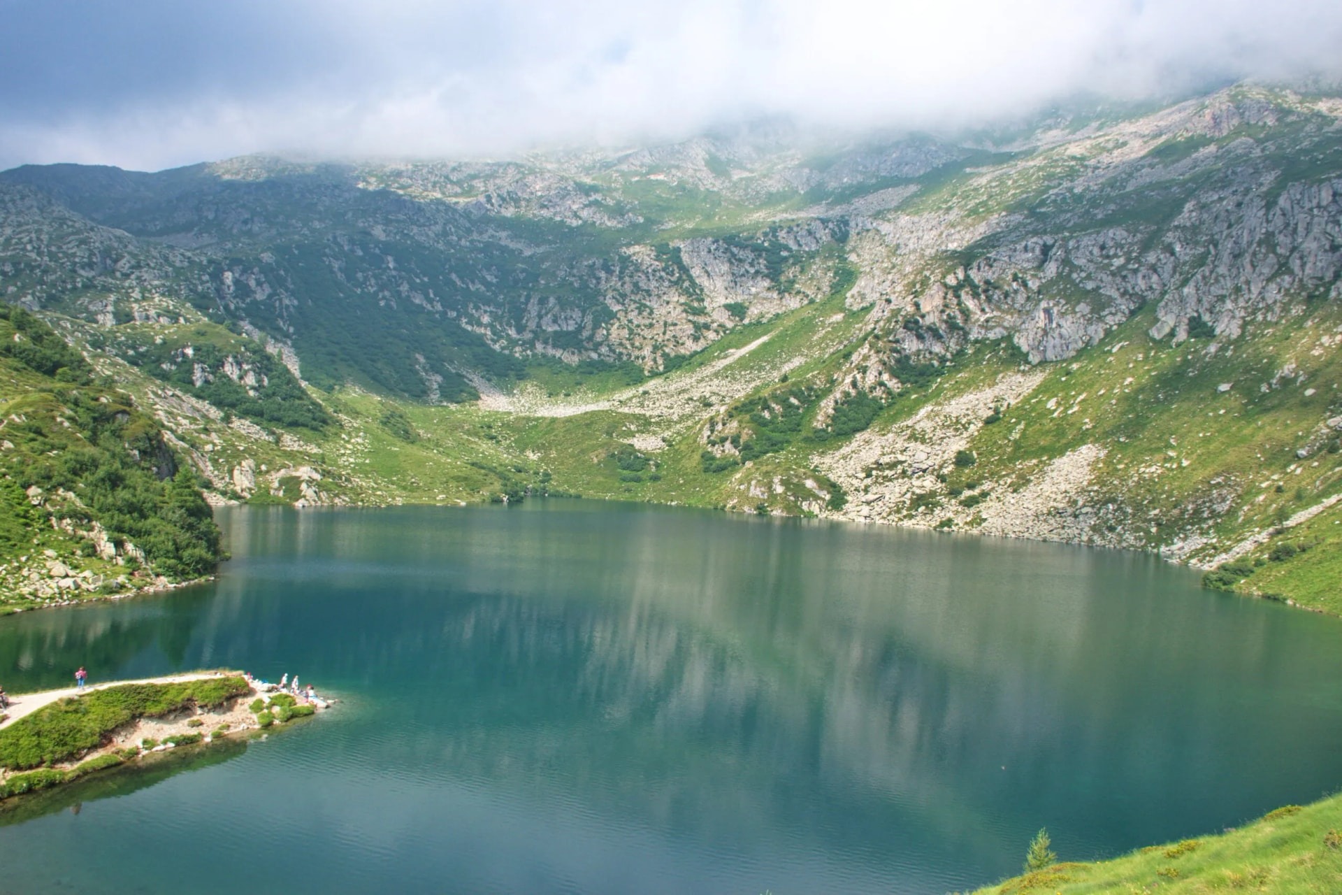 High-angle view of five lakes in Brenta Dolomites, Italy, with green slopes and misty peaks.
