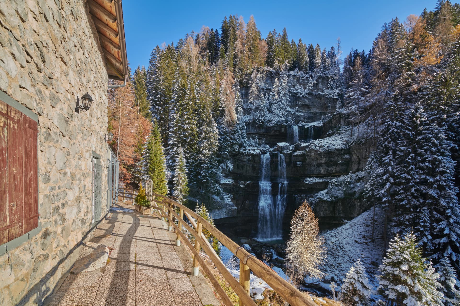 Waterfall in Vallesinella, Madonna di Campiglio, with autumn foliage and snow on evergreen trees.