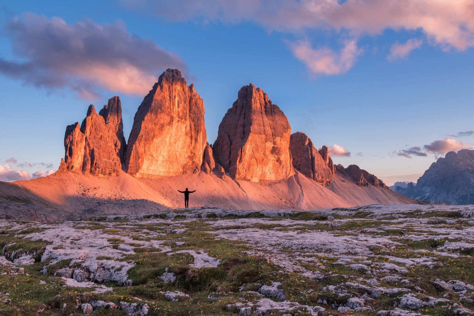 Hiker with arms outstretched before Tre Cime di Lavaredo in the Dolomites mountains at sunset.